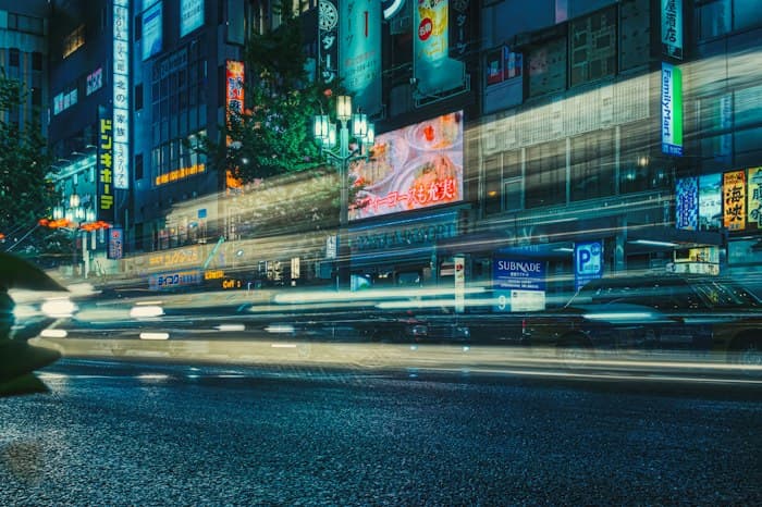 Bright signs lining a street at night, with light trails from passing cars